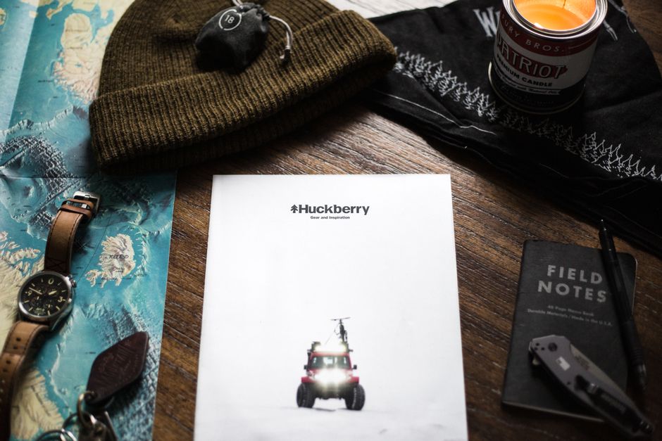 Creative flat lay of adventure gear and Huckberry magazine on a wooden surface.